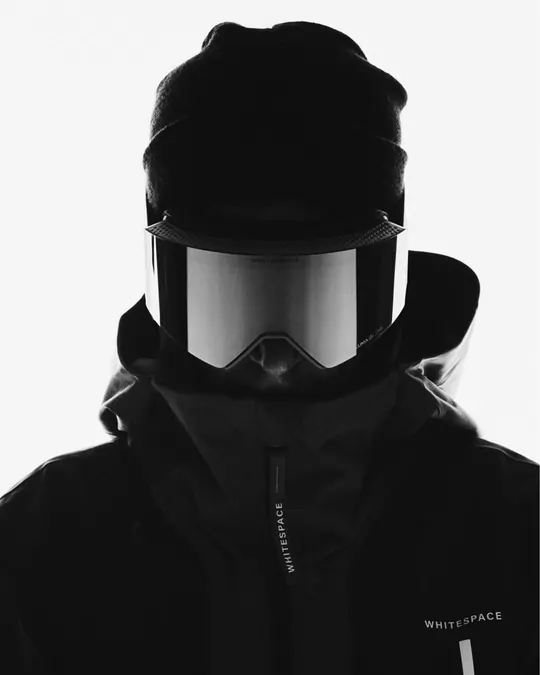 Rider in a black beanie, ski goggles and technical shell jacket