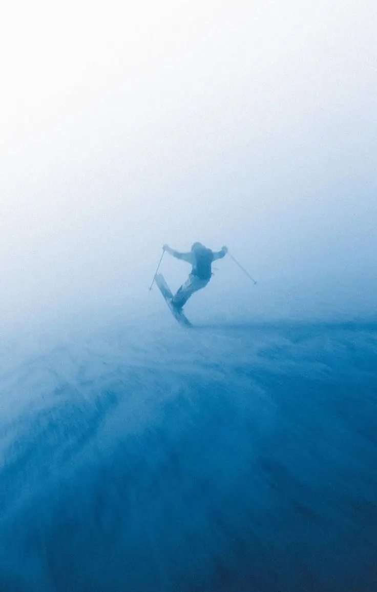 Skier turning through glacier-blue fog on an alpine slope